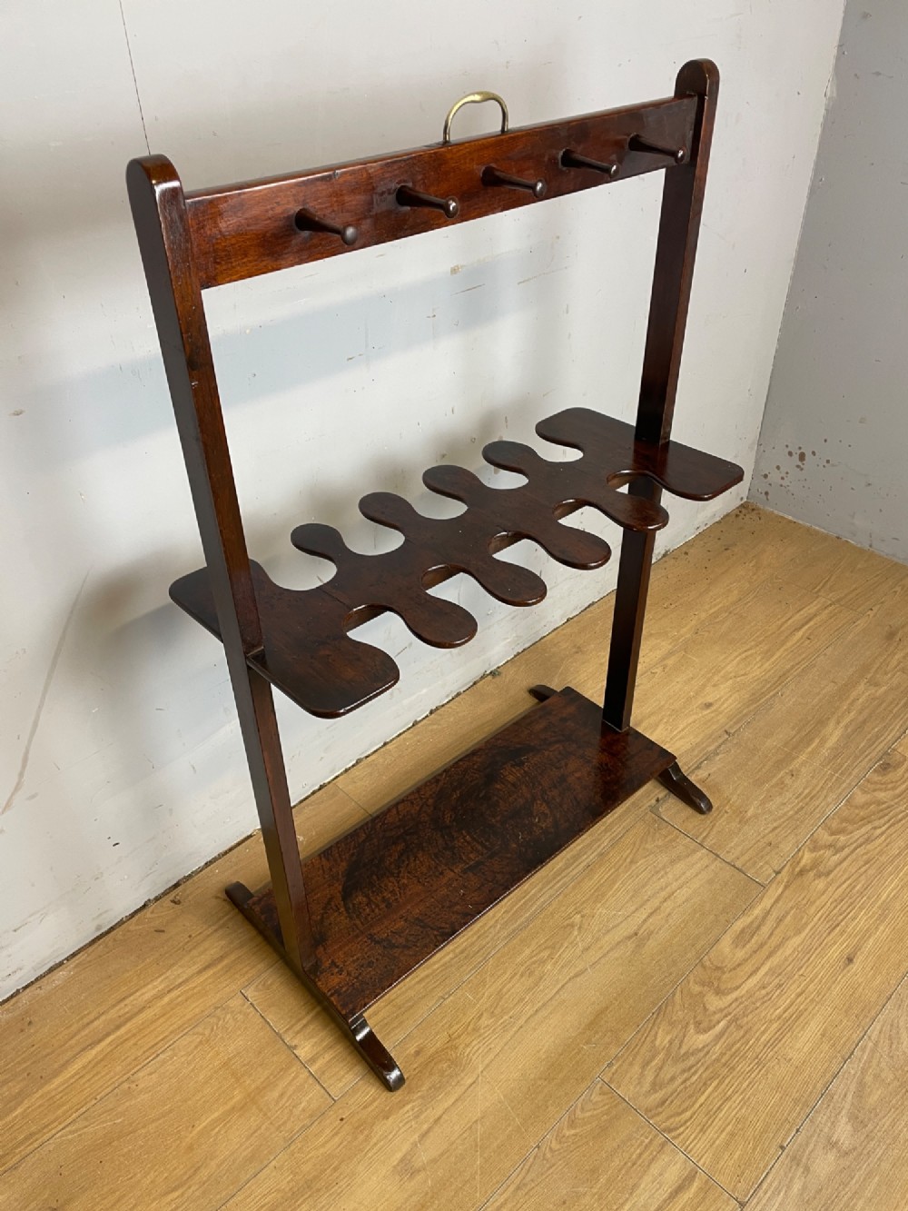 A dark mahogany Georgian boot and whip rack featuring an upper row of turned pegs, a brass handle, a central cutout shelf, and a solid base. View IX