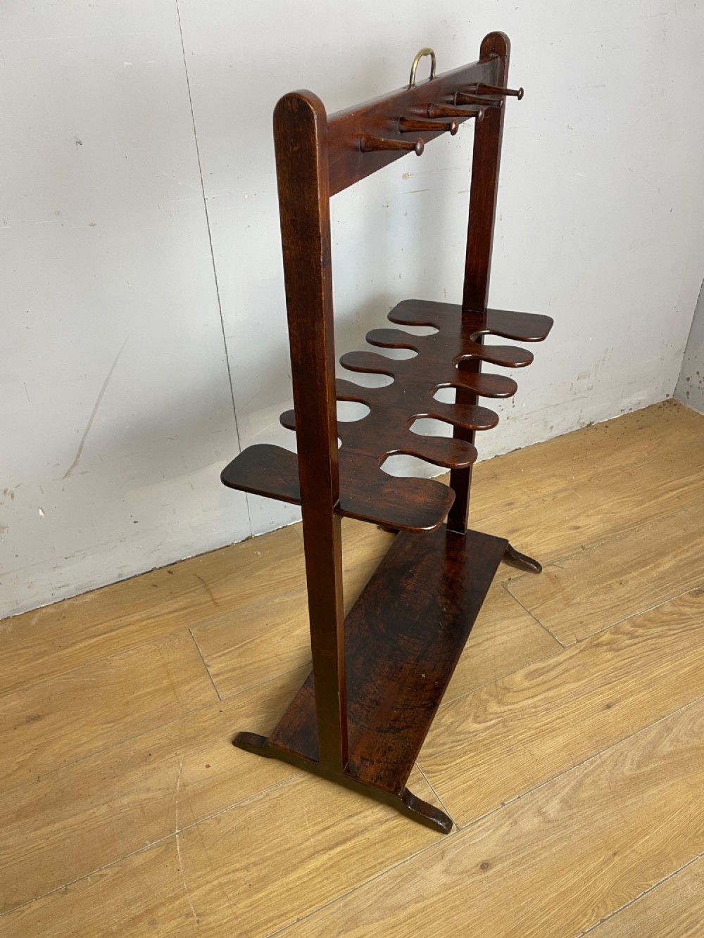 A dark mahogany Georgian boot and whip rack featuring an upper row of turned pegs, a brass handle, a central cutout shelf, and a solid base. View XI