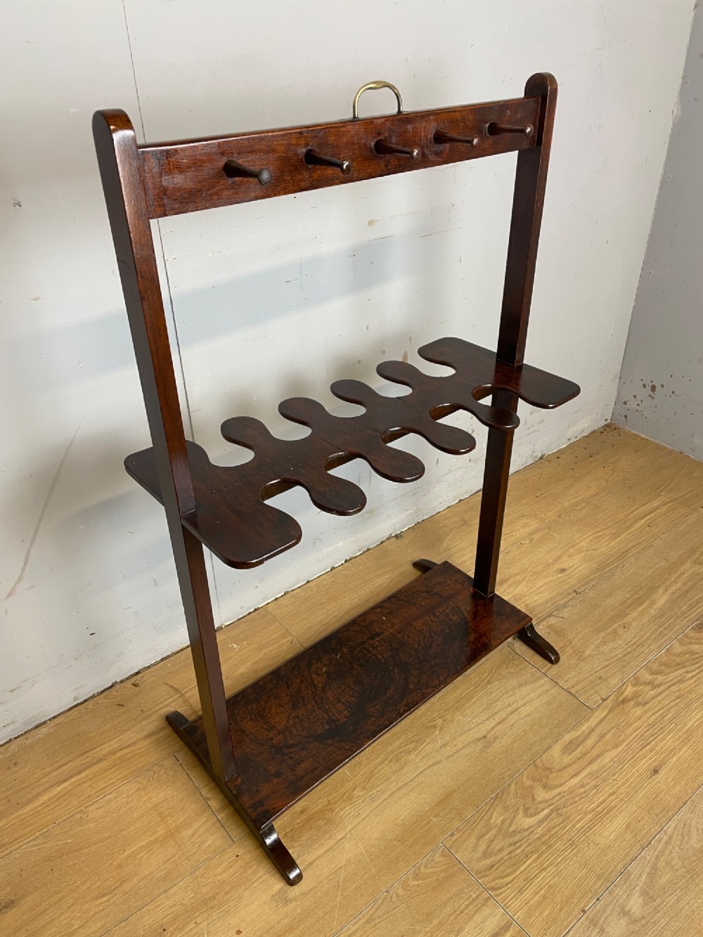 A dark mahogany Georgian boot and whip rack featuring an upper row of turned pegs, a brass handle, a central cutout shelf, and a solid base. View XII