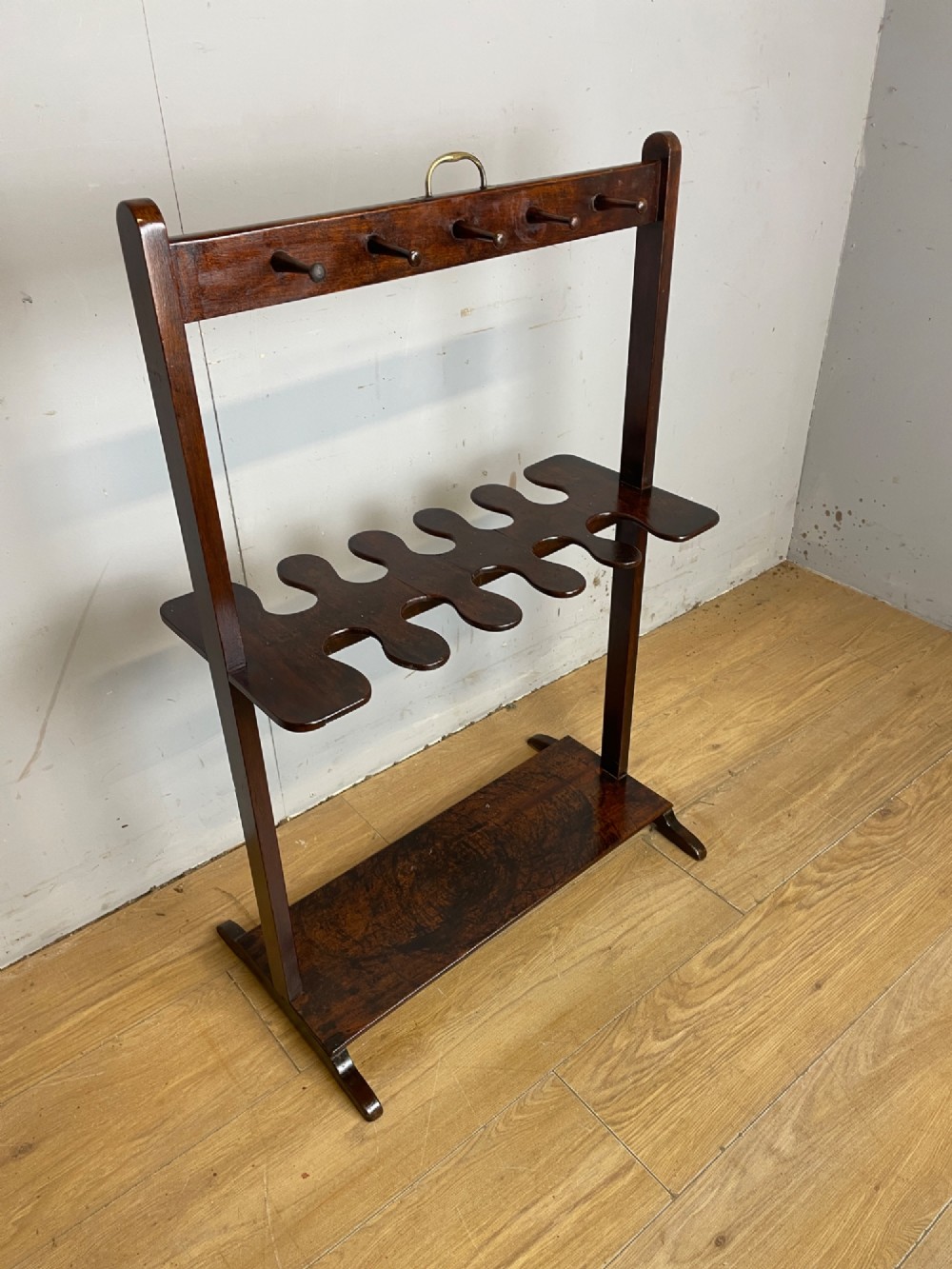 A dark mahogany Georgian boot and whip rack featuring an upper row of turned pegs, a brass handle, a central cutout shelf, and a solid base. View XIII