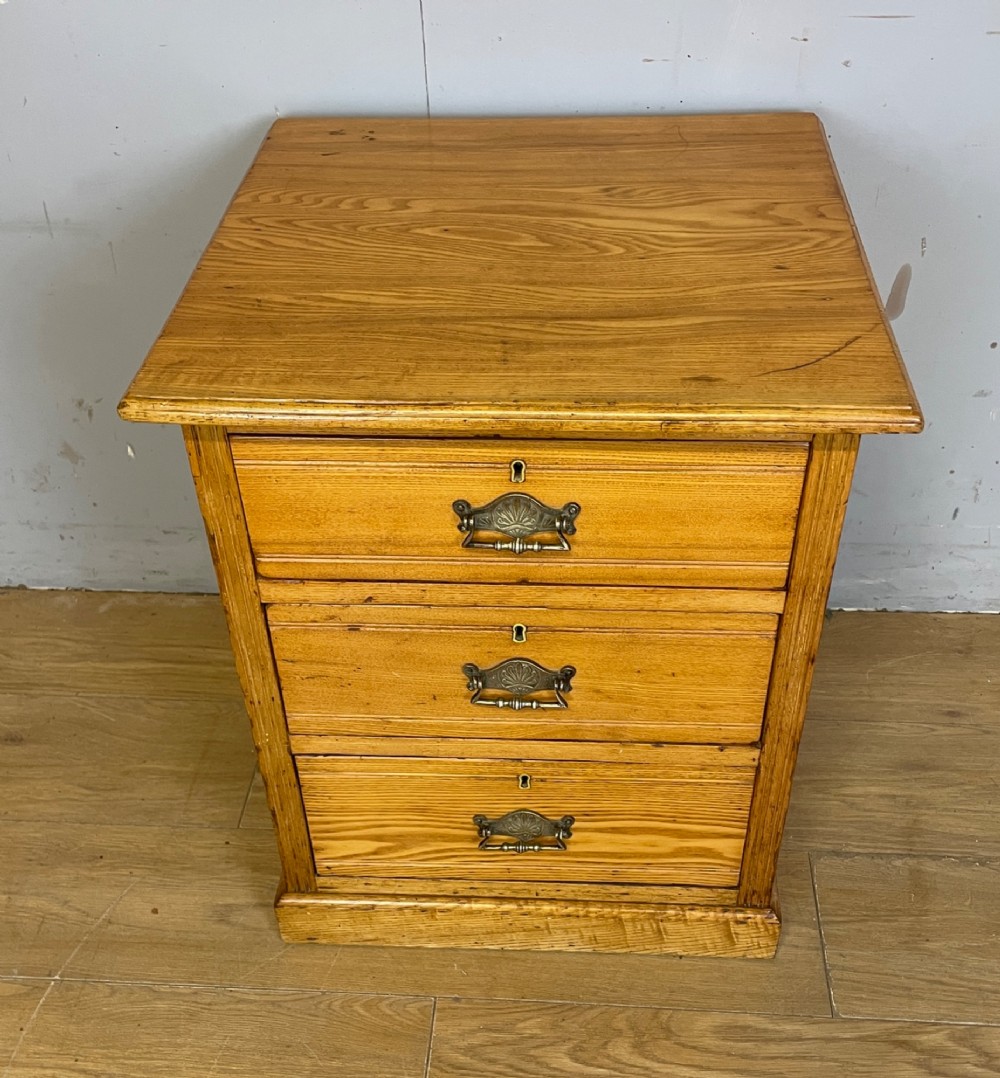 A late 19th-century small ash three-drawer chest featuring cast metal handles, brass keyhole escutcheons, a moulded edge top, and a solid plinth base. View II