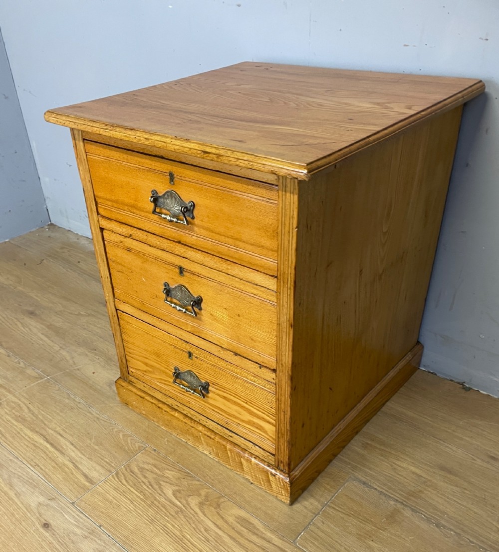 A late 19th-century small ash three-drawer chest featuring cast metal handles, brass keyhole escutcheons, a moulded edge top, and a solid plinth base. View III