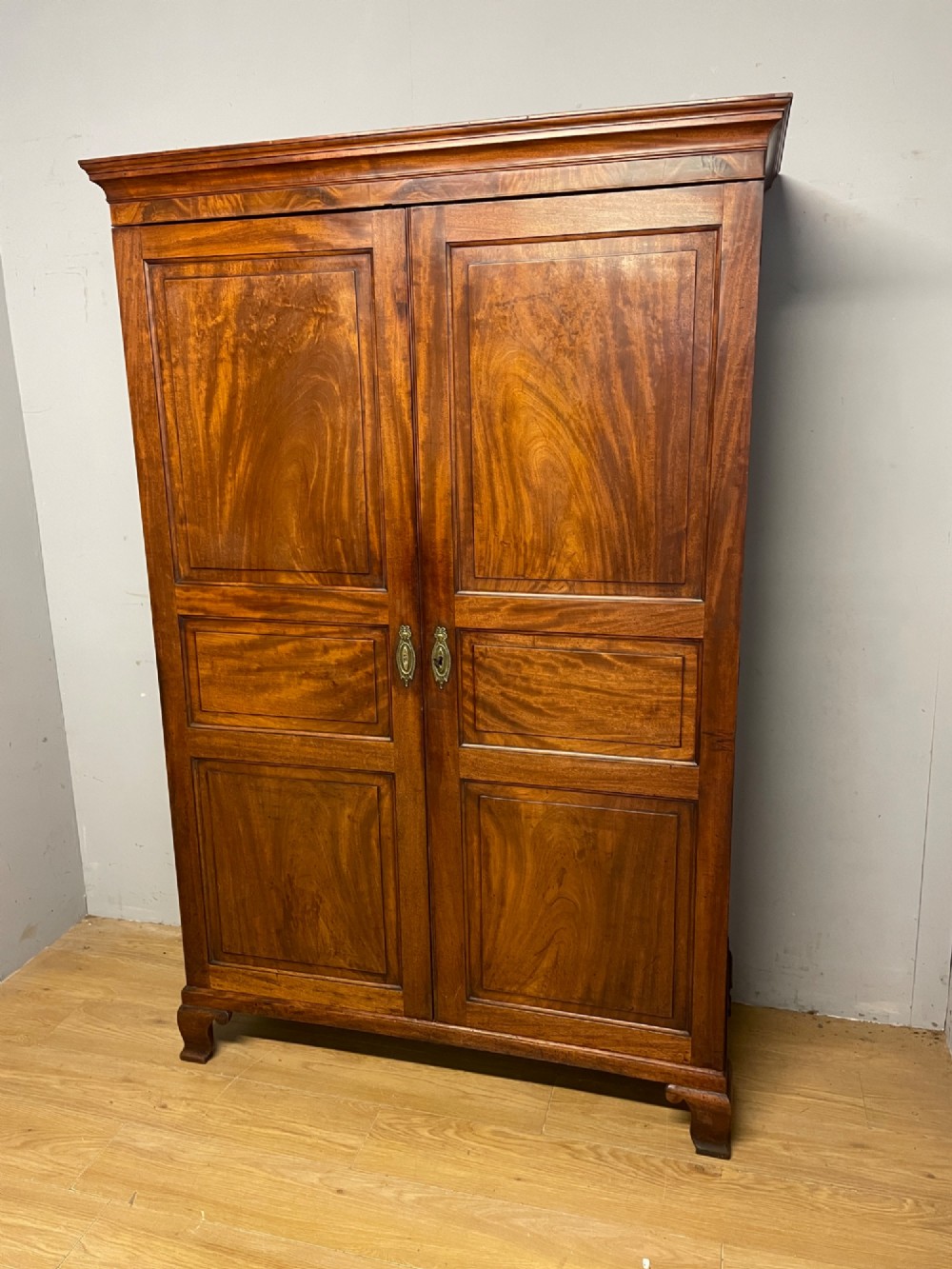 A nineteenth-century two-door flame mahogany wardrobe with panelled doors, brass escutcheons, and a moulded cornice.
