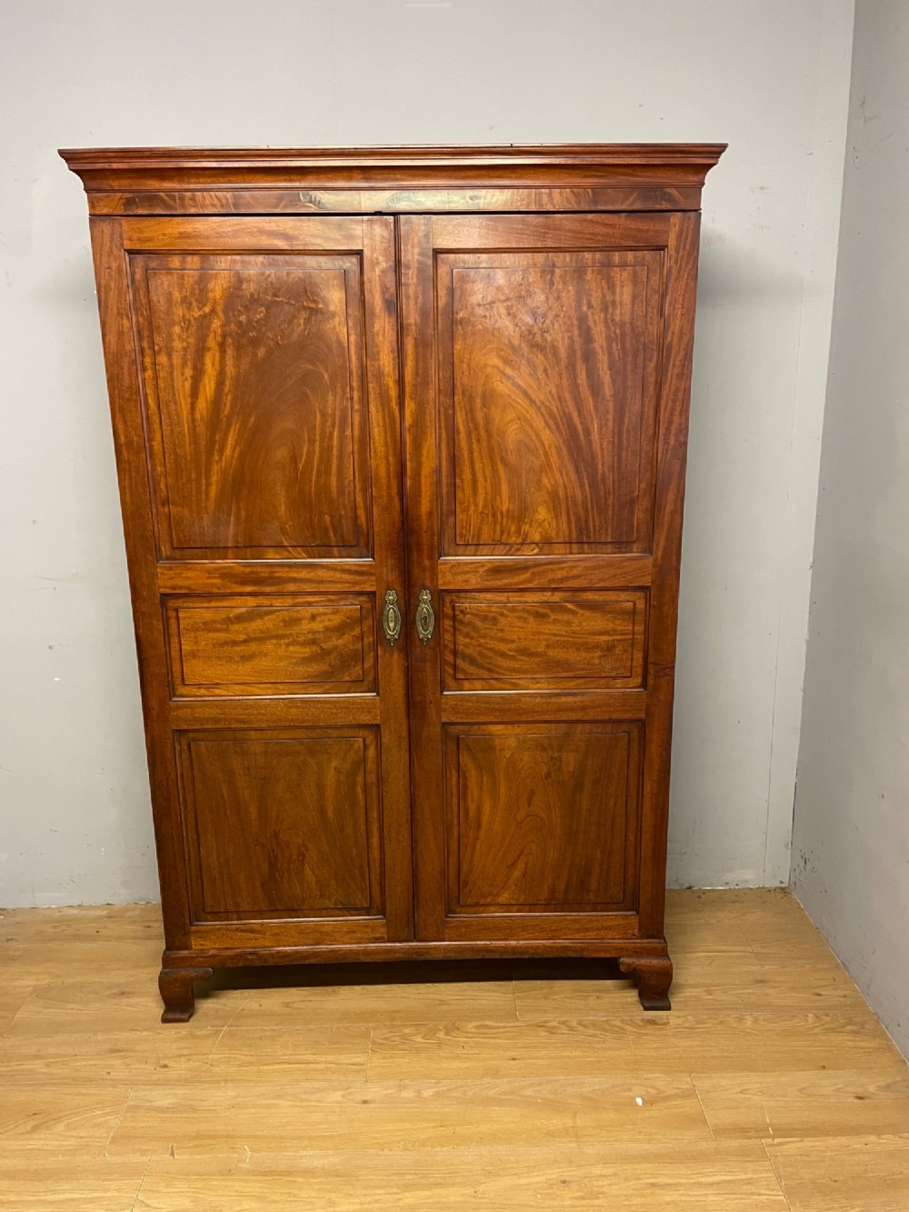 A nineteenth-century two-door flame mahogany wardrobe with panelled doors, brass escutcheons, and a moulded cornice. View II