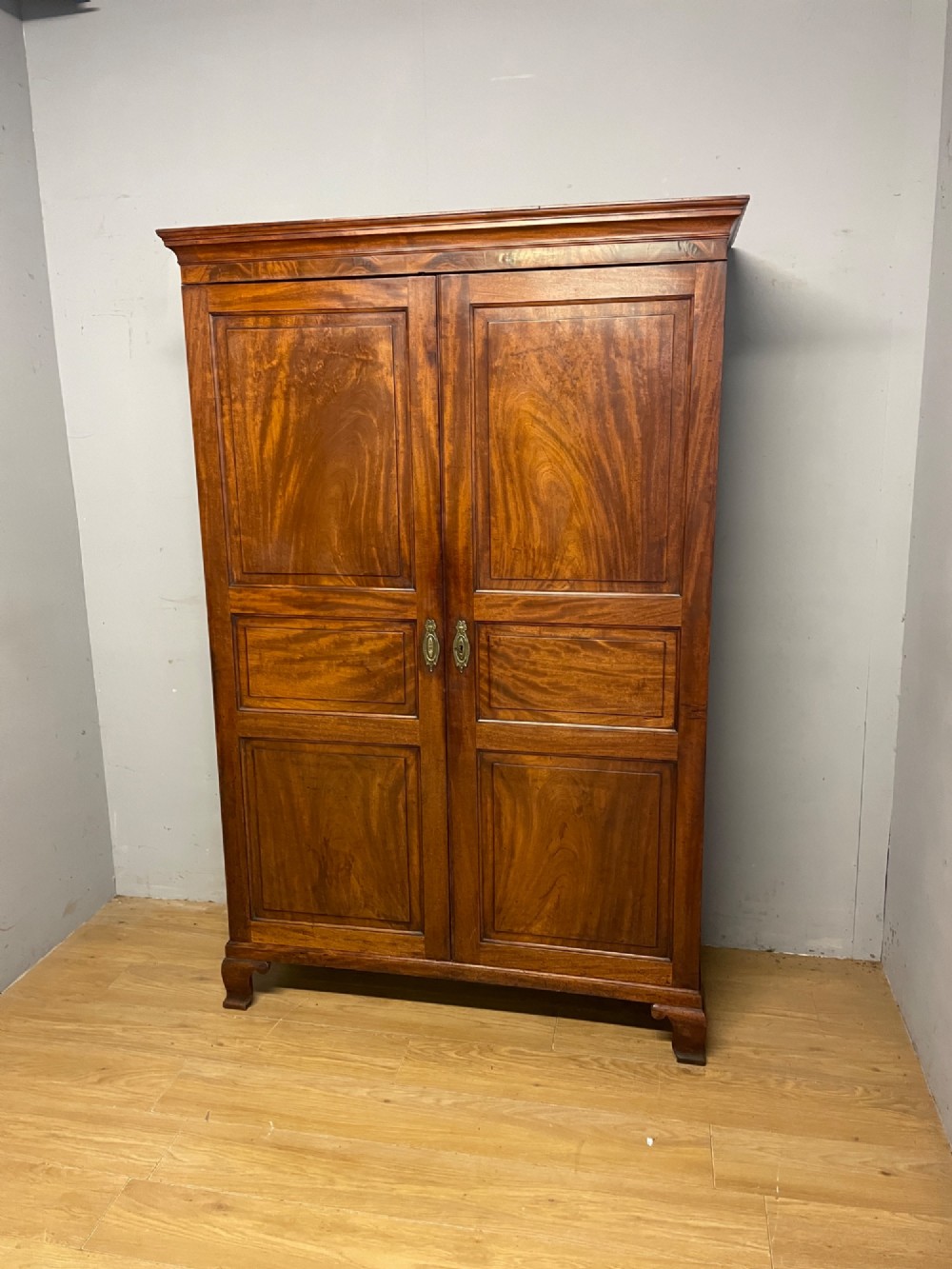 A nineteenth-century two-door flame mahogany wardrobe with panelled doors, brass escutcheons, and a moulded cornice. View XII