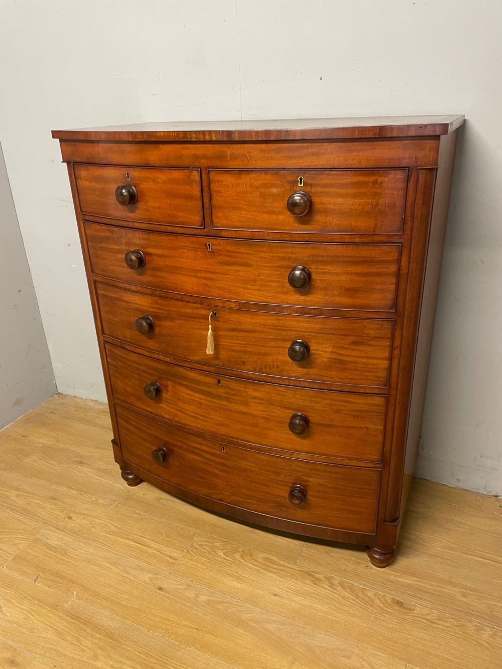 A 19th-century mahogany bow front chest of drawers featuring two short drawers over three long drawers with turned wooden handles.