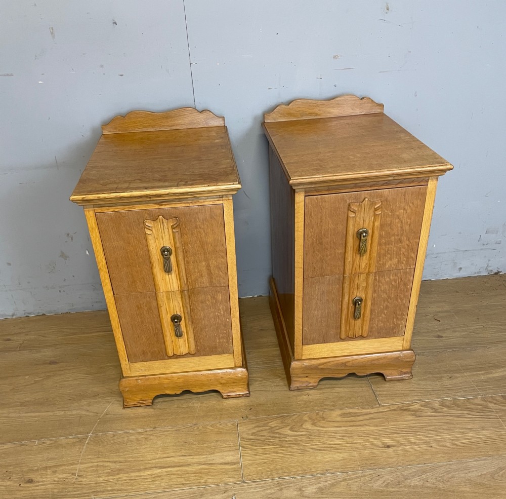 A pair of golden oak Art Deco bedside cabinets featuring two drawers each with stylized carved accents, drop handles, and a low curved back gallery. View II