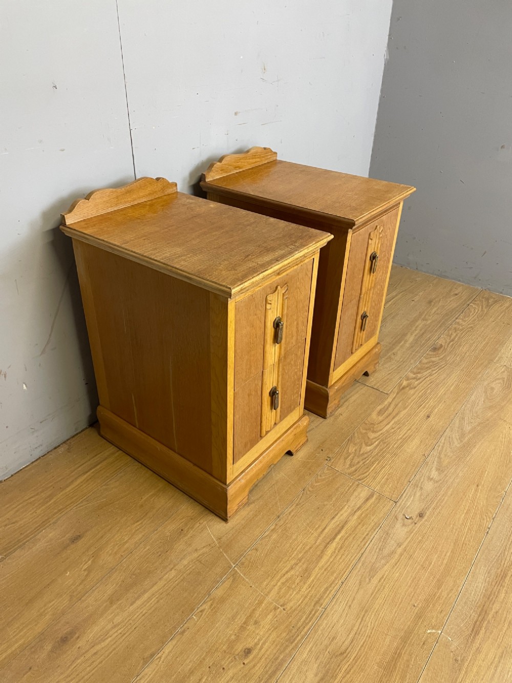 A pair of golden oak Art Deco bedside cabinets featuring two drawers each with stylized carved accents, drop handles, and a low curved back gallery. View III