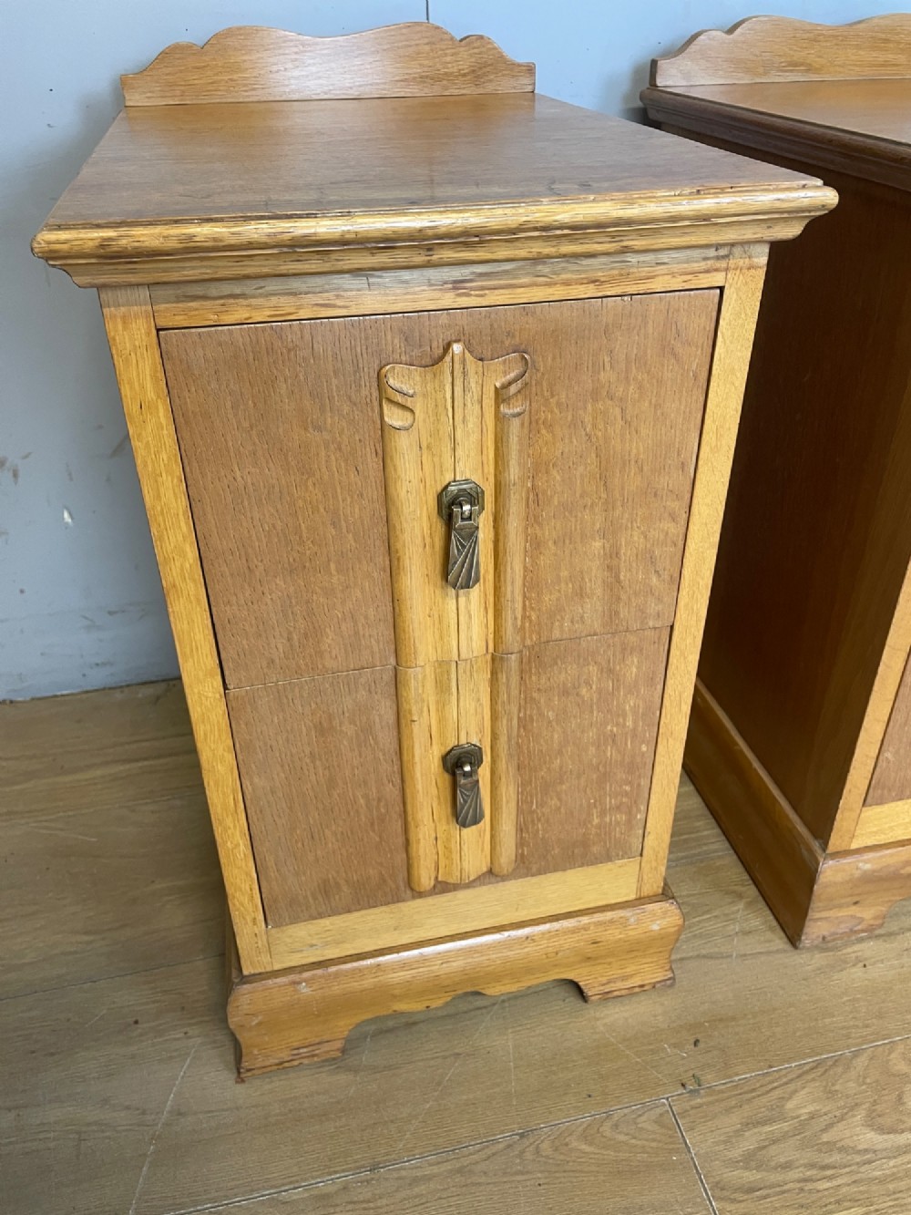 A pair of golden oak Art Deco bedside cabinets featuring two drawers each with stylized carved accents, drop handles, and a low curved back gallery. View IV