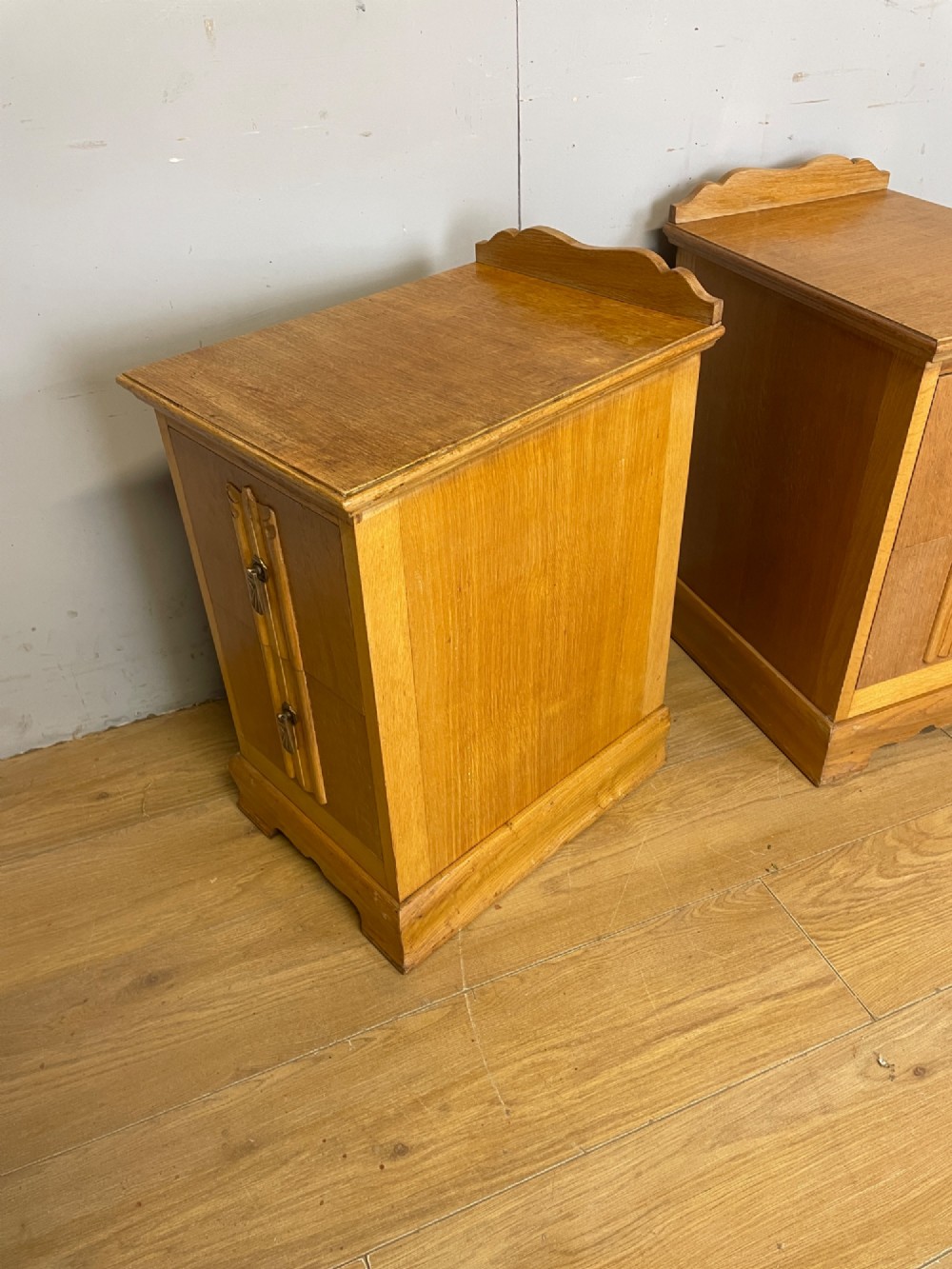 A pair of golden oak Art Deco bedside cabinets featuring two drawers each with stylized carved accents, drop handles, and a low curved back gallery. View V