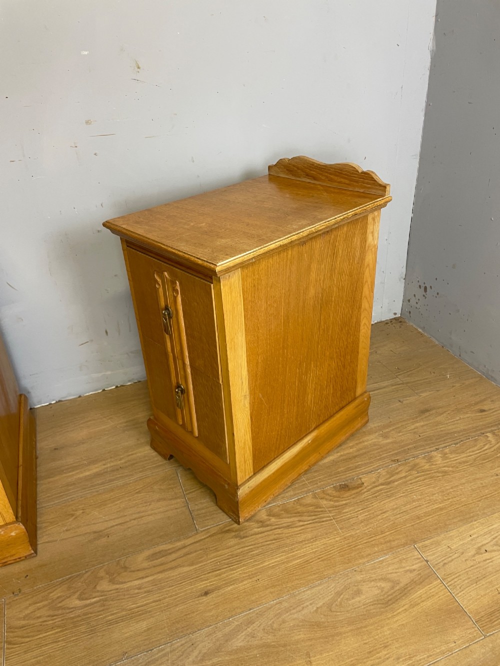 A pair of golden oak Art Deco bedside cabinets featuring two drawers each with stylized carved accents, drop handles, and a low curved back gallery. View VIII