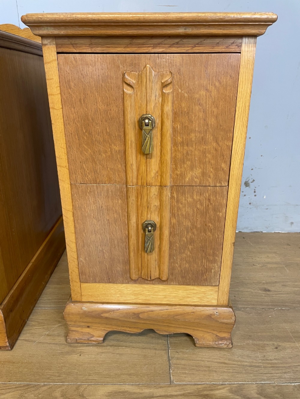 A pair of golden oak Art Deco bedside cabinets featuring two drawers each with stylized carved accents, drop handles, and a low curved back gallery. View IX