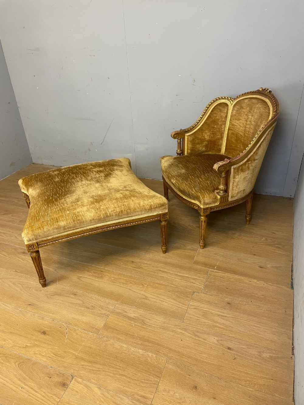An Edwardian carved giltwood armchair with a matching rectangular footstool upholstered in gold velvet.