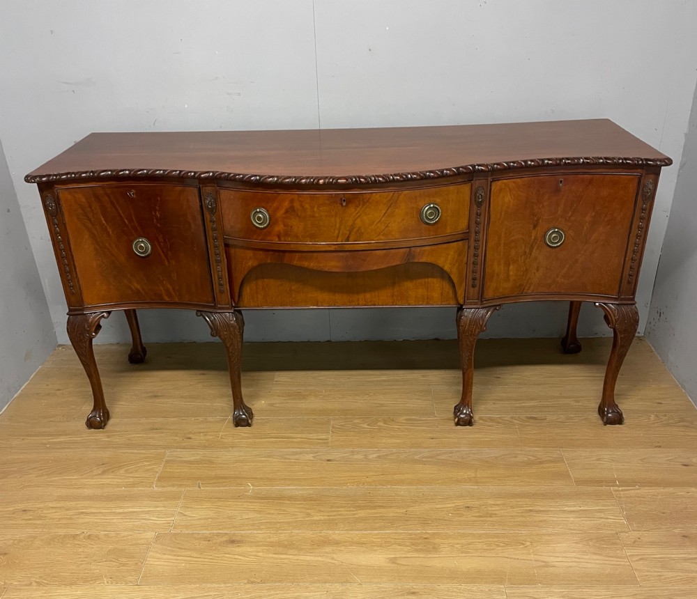 A late 19th-century flame mahogany Chippendale revival sideboard featuring carved cabriole legs with ball-and-claw feet, serpentine front drawers, and brass ring handles. View II