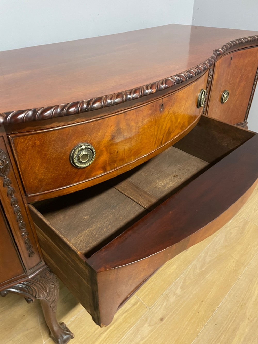 A late 19th-century flame mahogany Chippendale revival sideboard featuring carved cabriole legs with ball-and-claw feet, serpentine front drawers, and brass ring handles. View VIII