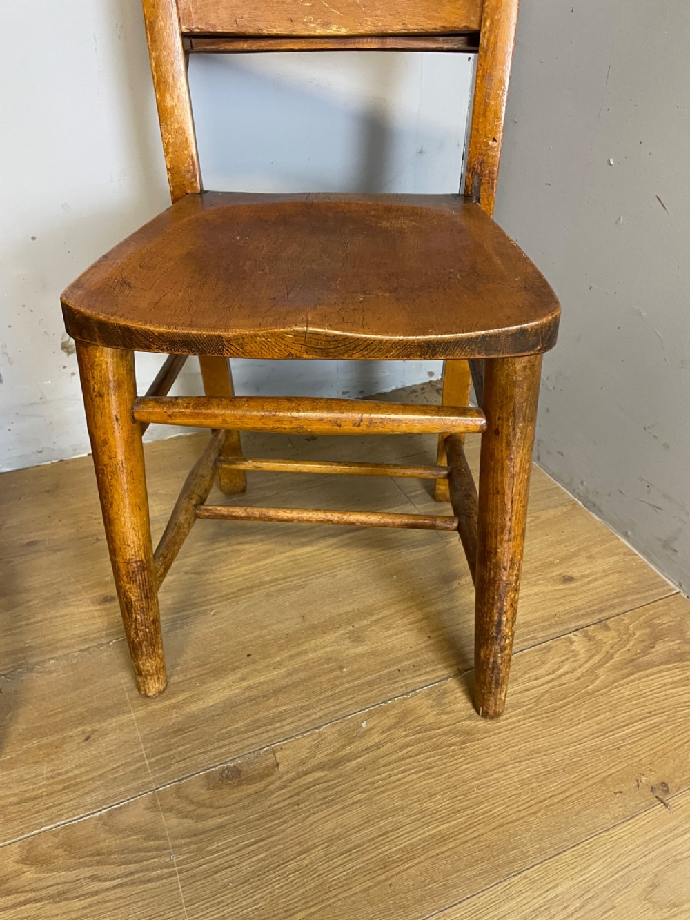 A set of four late nineteenth-century wooden chapel chairs featuring solid elm seats, open backrests with integrated bible troughs, and sturdy stretchers. View V