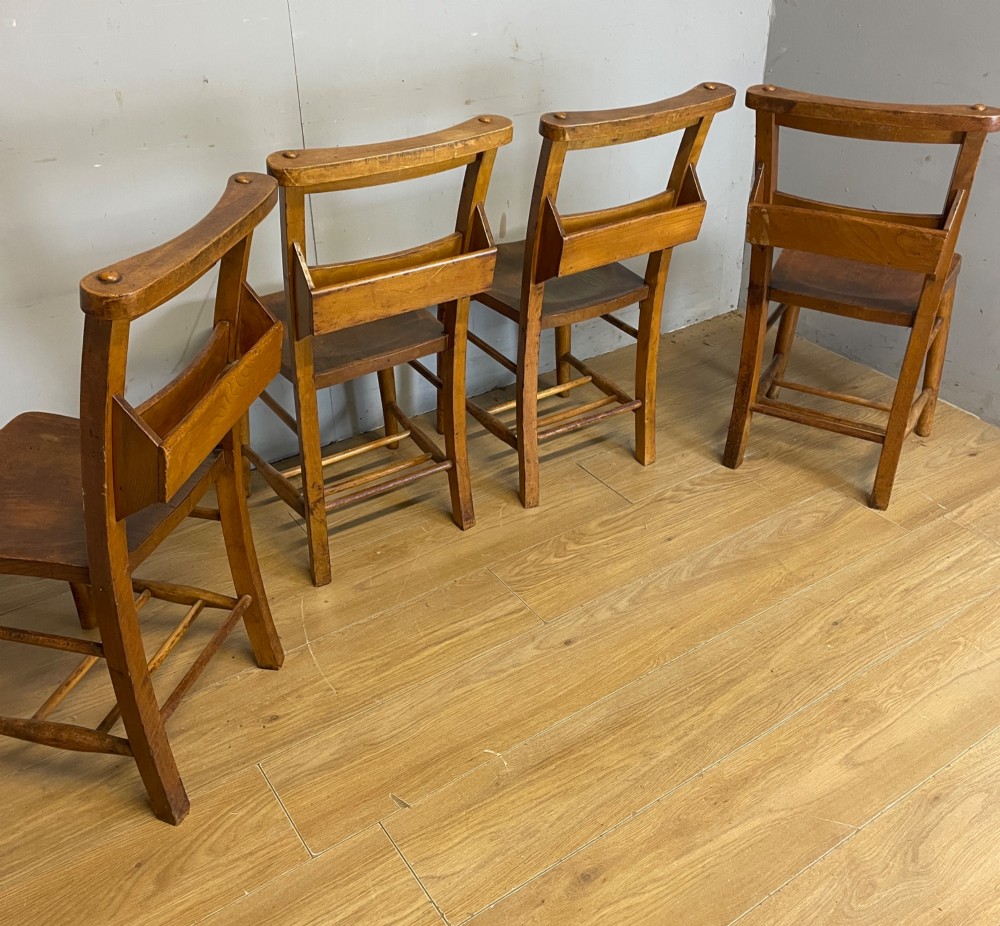 A set of four late nineteenth-century wooden chapel chairs featuring solid elm seats, open backrests with integrated bible troughs, and sturdy stretchers. View VI