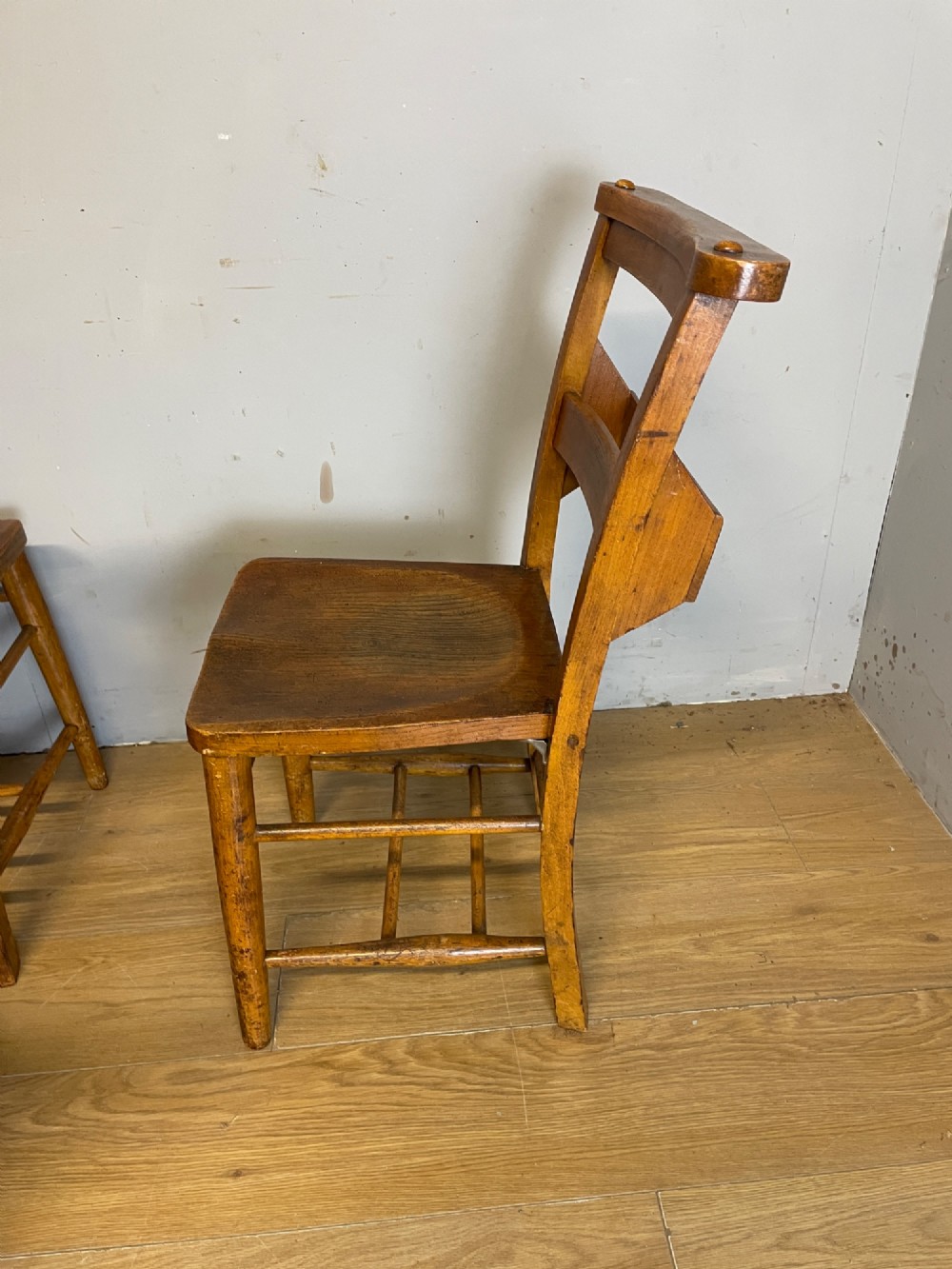 A set of four late nineteenth-century wooden chapel chairs featuring solid elm seats, open backrests with integrated bible troughs, and sturdy stretchers. View VII