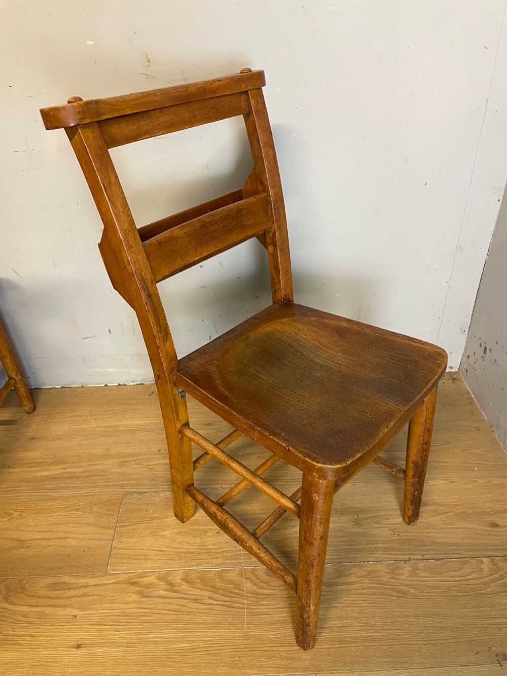 A set of four late nineteenth-century wooden chapel chairs featuring solid elm seats, open backrests with integrated bible troughs, and sturdy stretchers. View IX