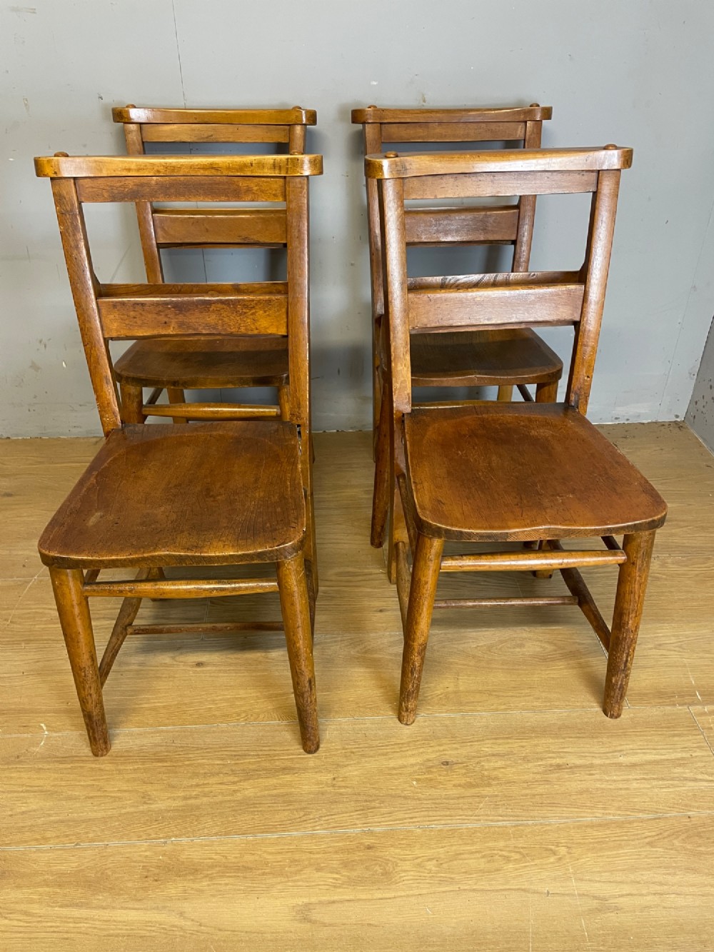 A set of four late nineteenth-century wooden chapel chairs featuring solid elm seats, open backrests with integrated bible troughs, and sturdy stretchers. View X