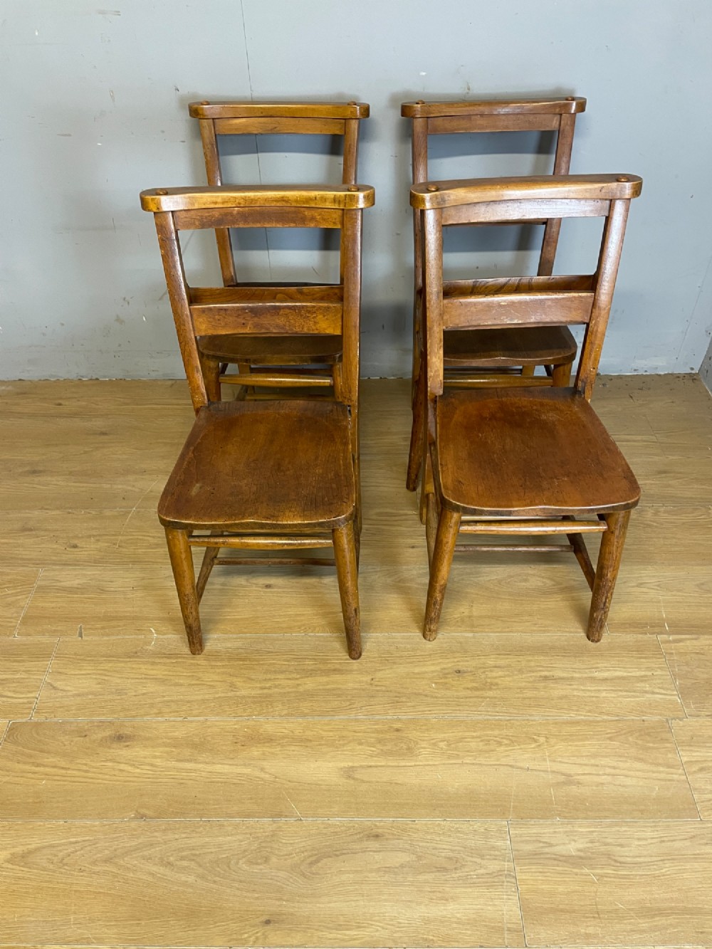 A set of four late nineteenth-century wooden chapel chairs featuring solid elm seats, open backrests with integrated bible troughs, and sturdy stretchers. View XI
