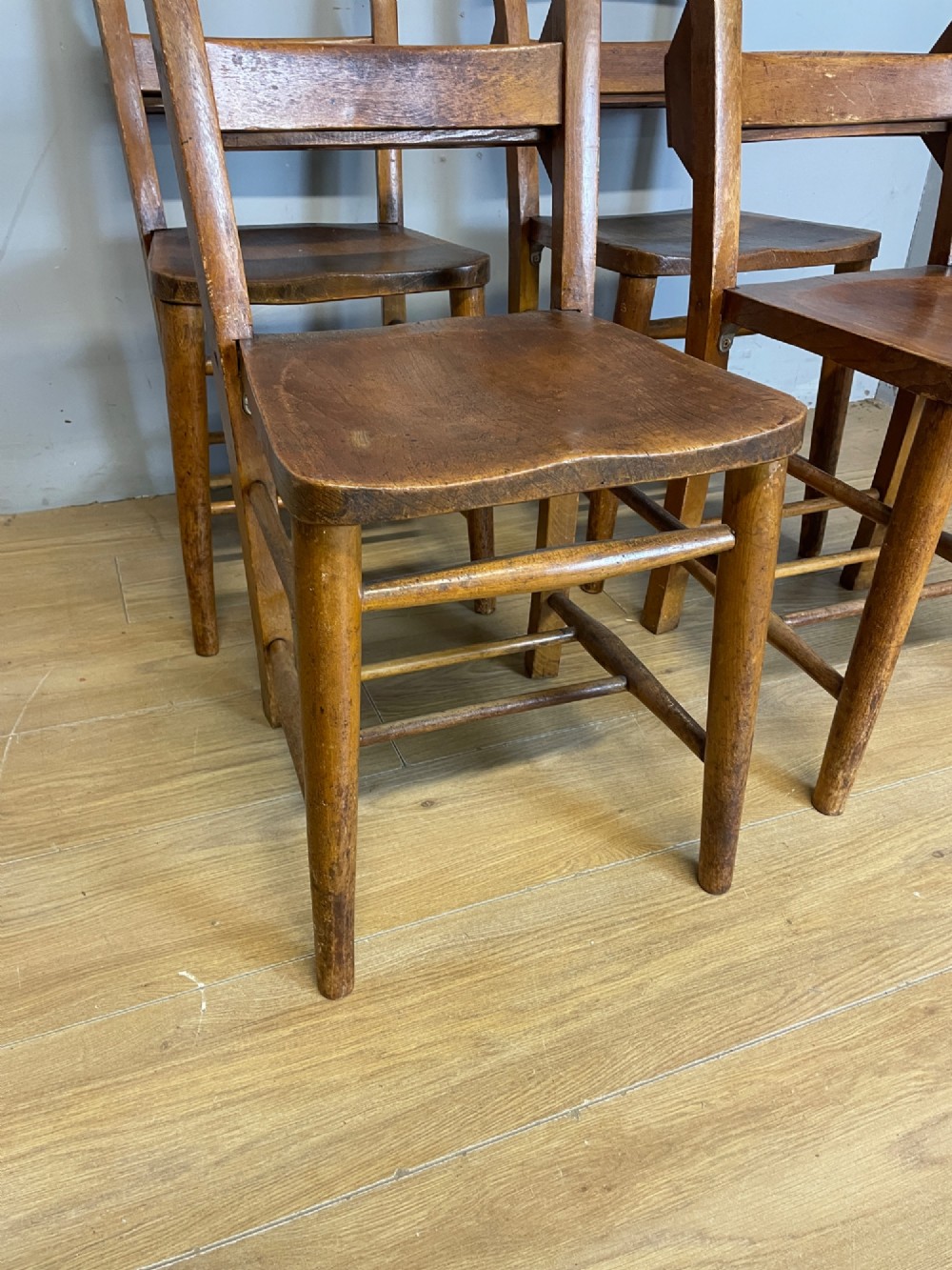 A set of four late nineteenth-century wooden chapel chairs featuring solid elm seats, open backrests with integrated bible troughs, and sturdy stretchers. View XII