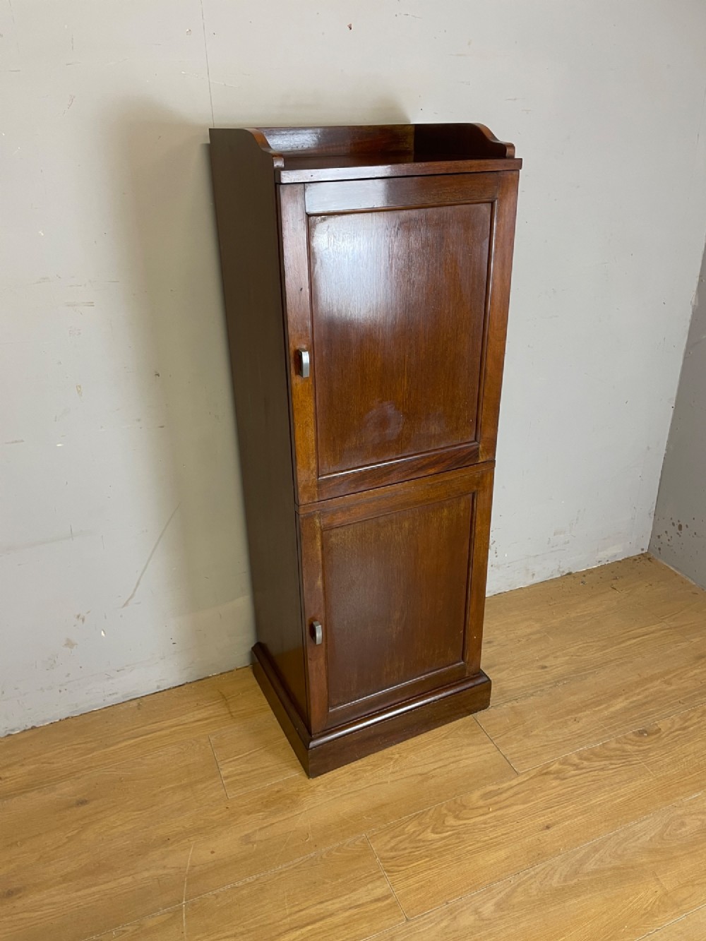 A tall, narrow early 20th-century solid mahogany filing cabinet featuring two panelled door drawers with metal handles, a plinth base, and a raised gallery top.