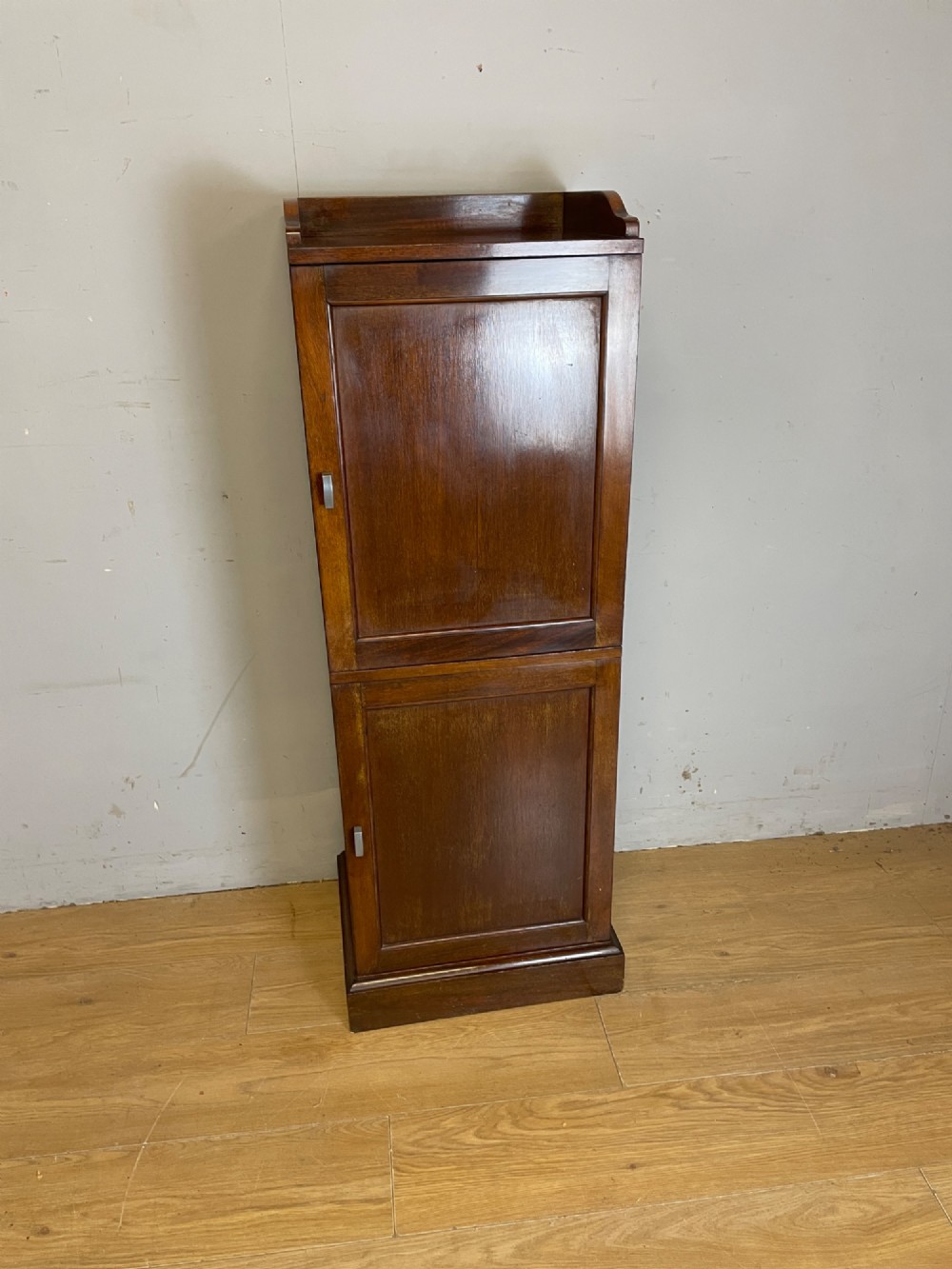 A tall, narrow early 20th-century solid mahogany filing cabinet featuring two panelled door drawers with metal handles, a plinth base, and a raised gallery top. View II