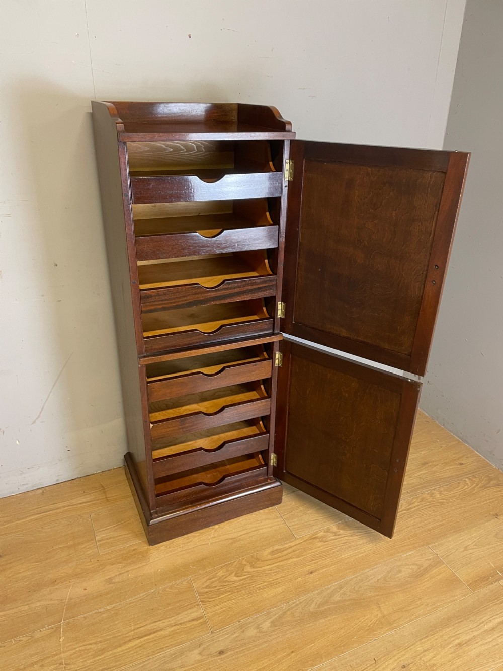 A tall, narrow early 20th-century solid mahogany filing cabinet featuring two panelled door drawers with metal handles, a plinth base, and a raised gallery top. View IV