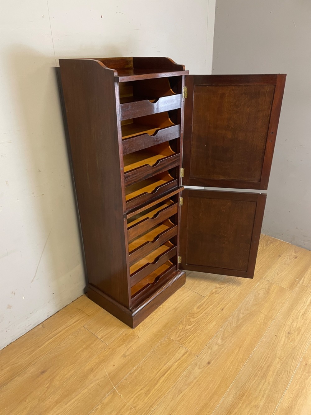 A tall, narrow early 20th-century solid mahogany filing cabinet featuring two panelled door drawers with metal handles, a plinth base, and a raised gallery top. View V