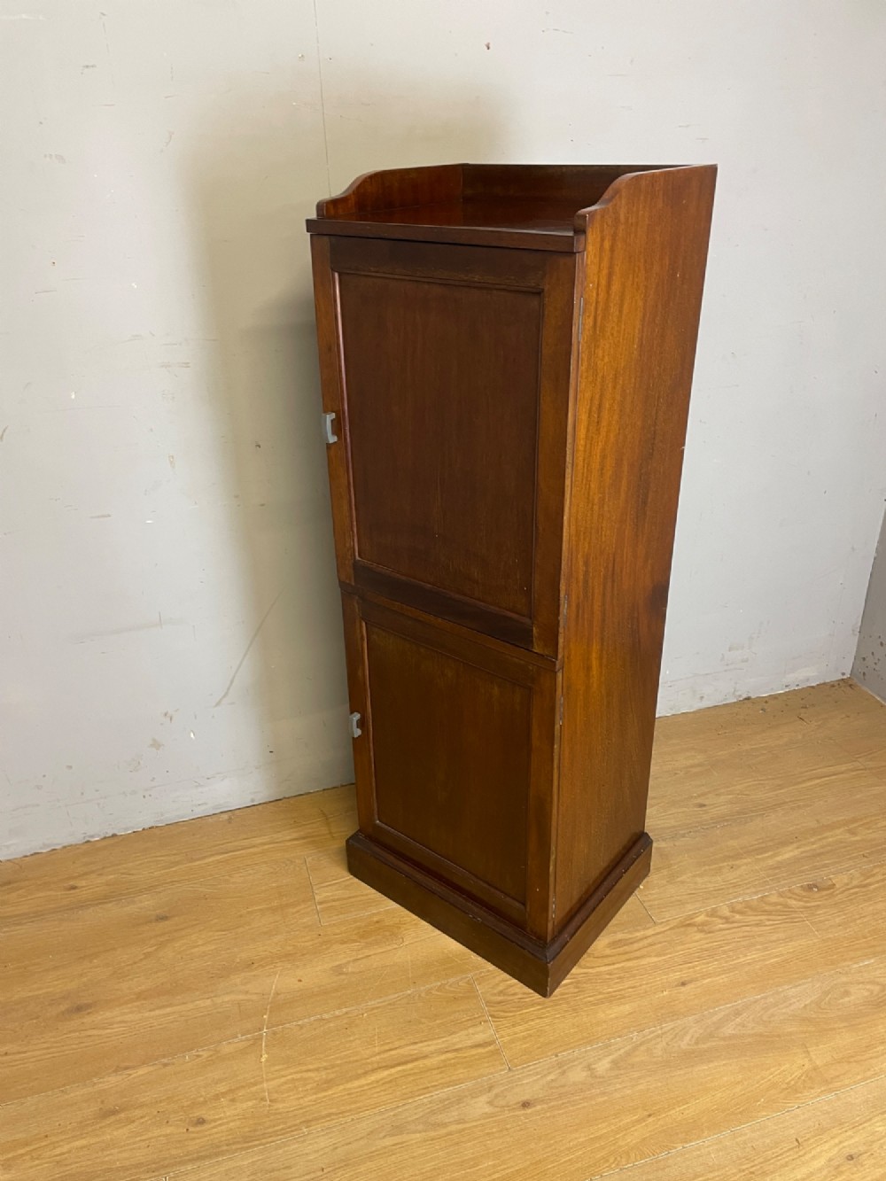 A tall, narrow early 20th-century solid mahogany filing cabinet featuring two panelled door drawers with metal handles, a plinth base, and a raised gallery top. View VI