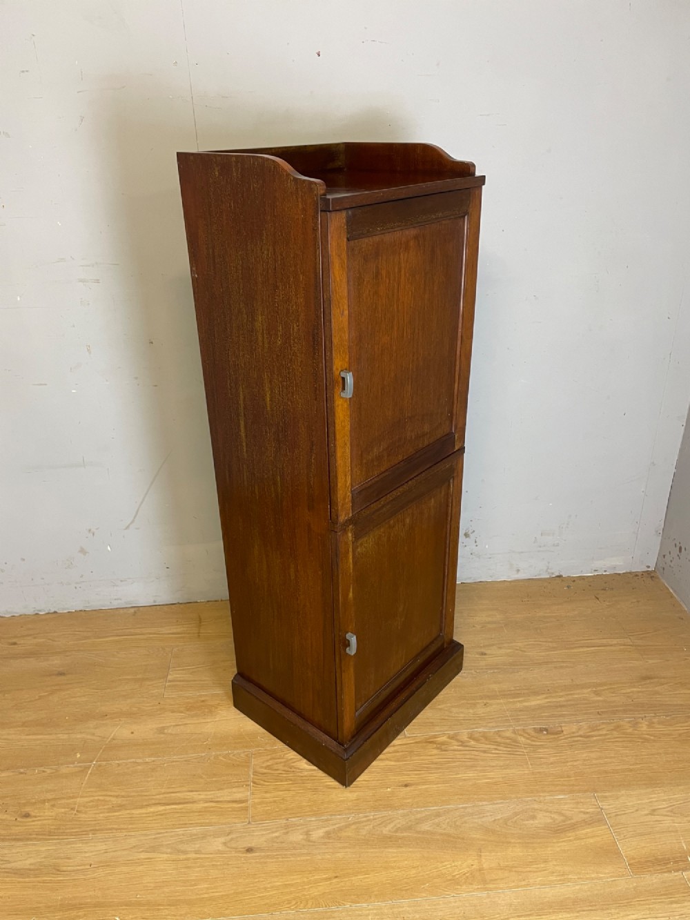 A tall, narrow early 20th-century solid mahogany filing cabinet featuring two panelled door drawers with metal handles, a plinth base, and a raised gallery top. View VII