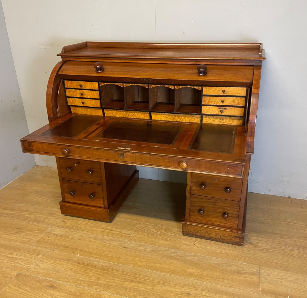 A nineteenth-century mahogany cylinder pedestal desk featuring a curved roll-down front, an extendable leather-lined writing slope, small interior drawers, and twin pedestals.