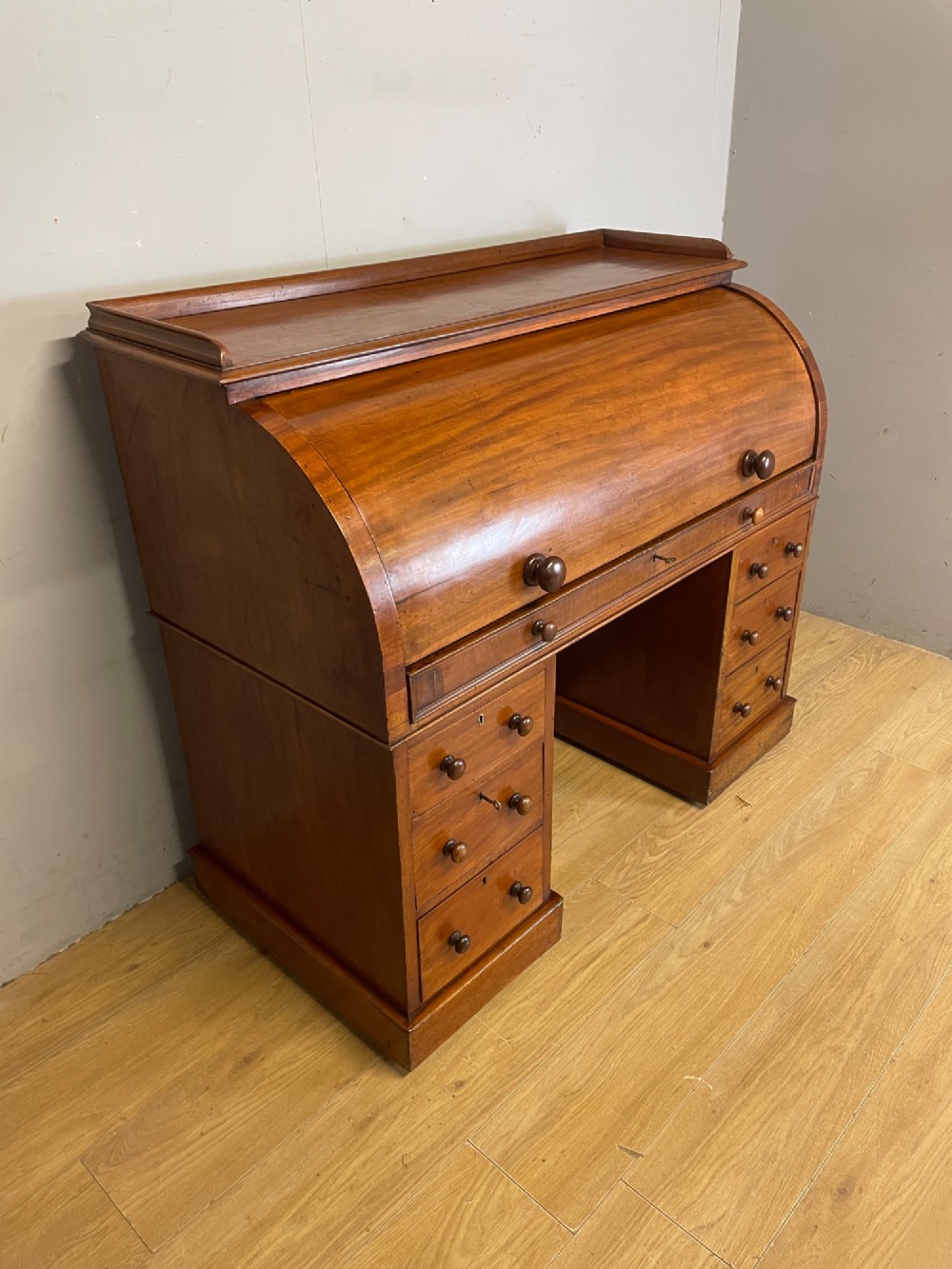 A nineteenth-century mahogany cylinder pedestal desk featuring a curved roll-down front, an extendable leather-lined writing slope, small interior drawers, and twin pedestals. View IV