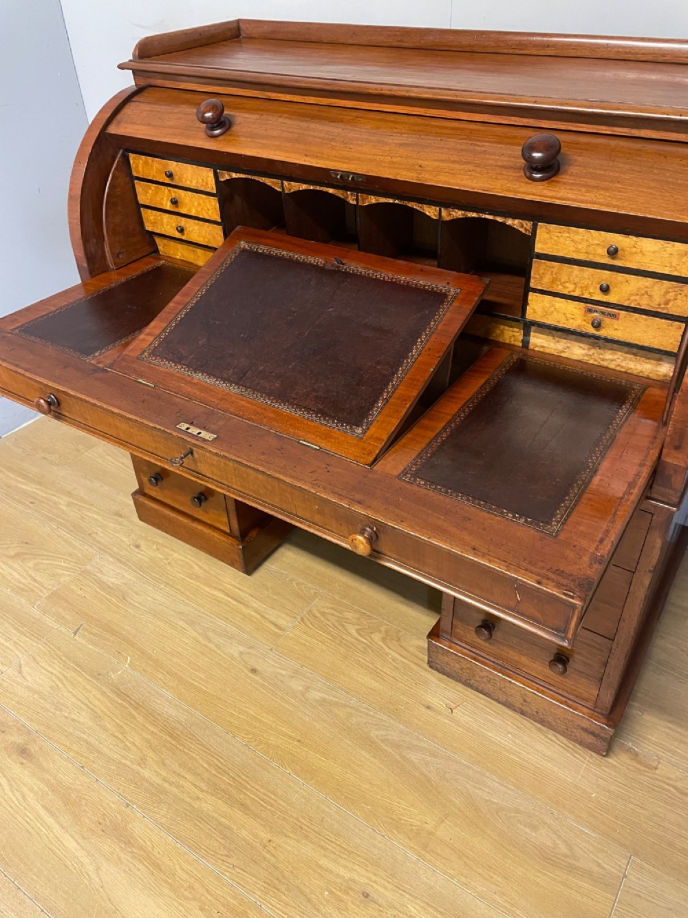 A nineteenth-century mahogany cylinder pedestal desk featuring a curved roll-down front, an extendable leather-lined writing slope, small interior drawers, and twin pedestals. View V