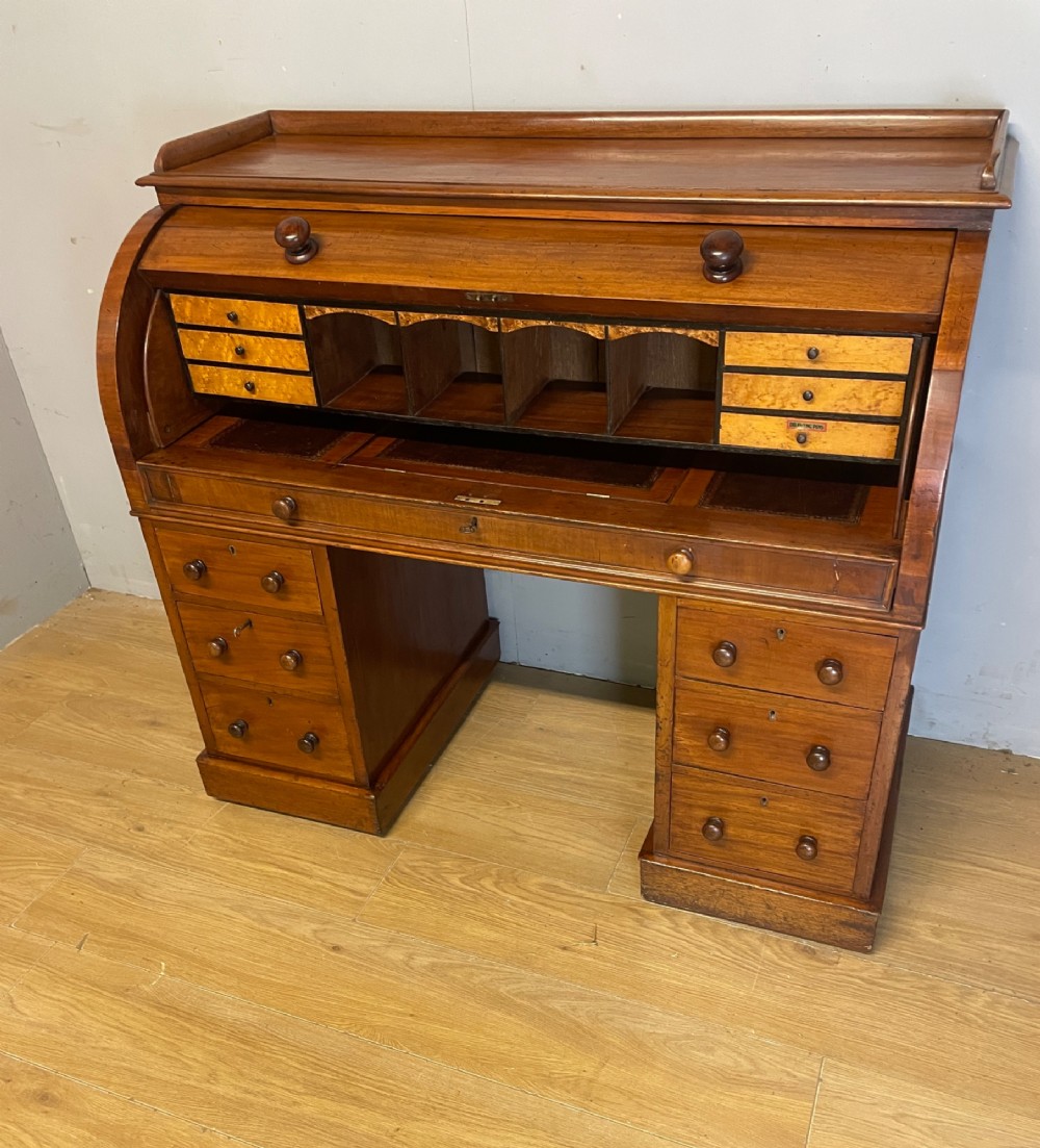 A nineteenth-century mahogany cylinder pedestal desk featuring a curved roll-down front, an extendable leather-lined writing slope, small interior drawers, and twin pedestals. View XI