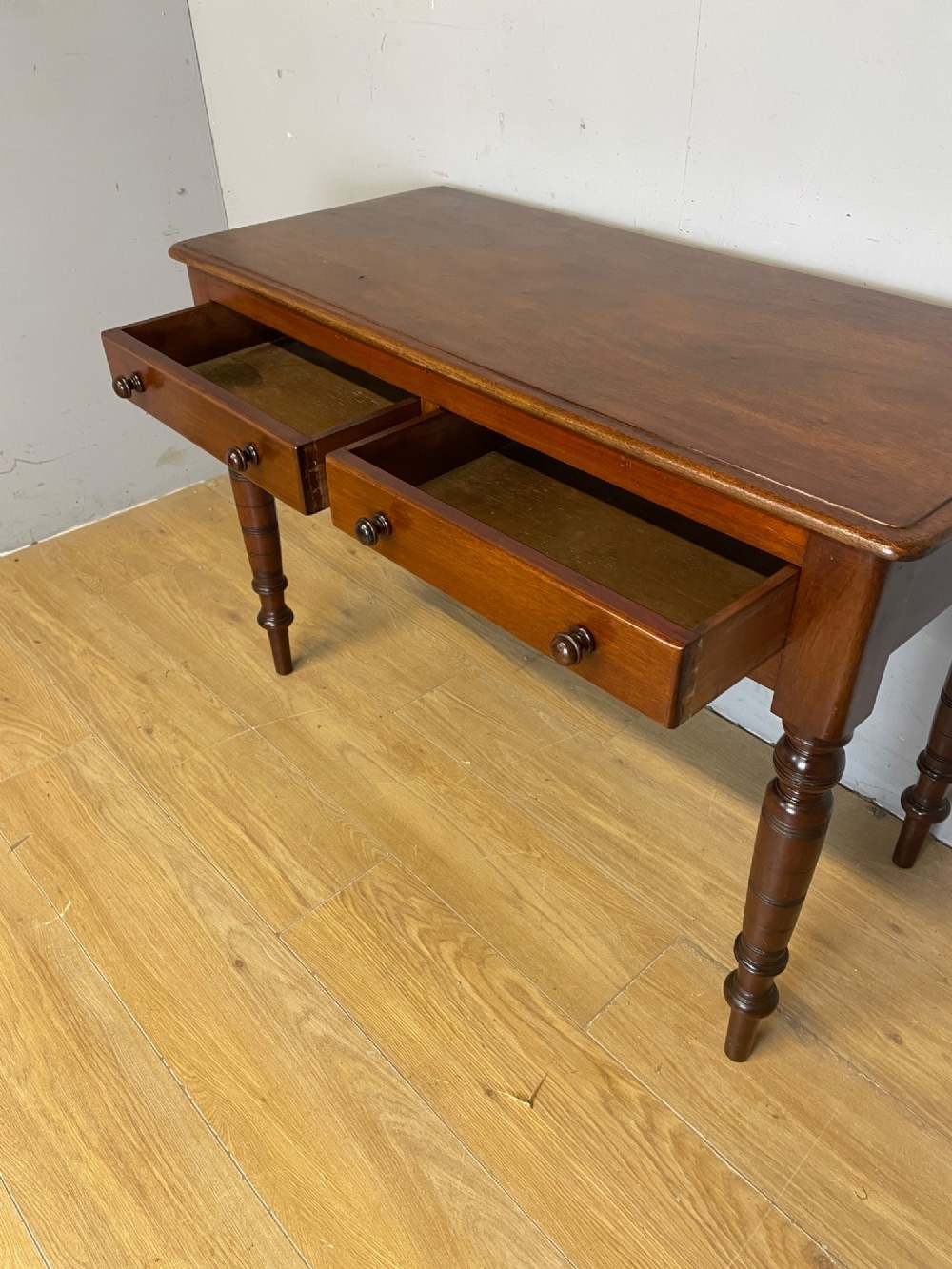 A 19th-century mahogany side table featuring a rectangular top, two front drawers with turned wooden knobs, and four ring-turned legs. View V