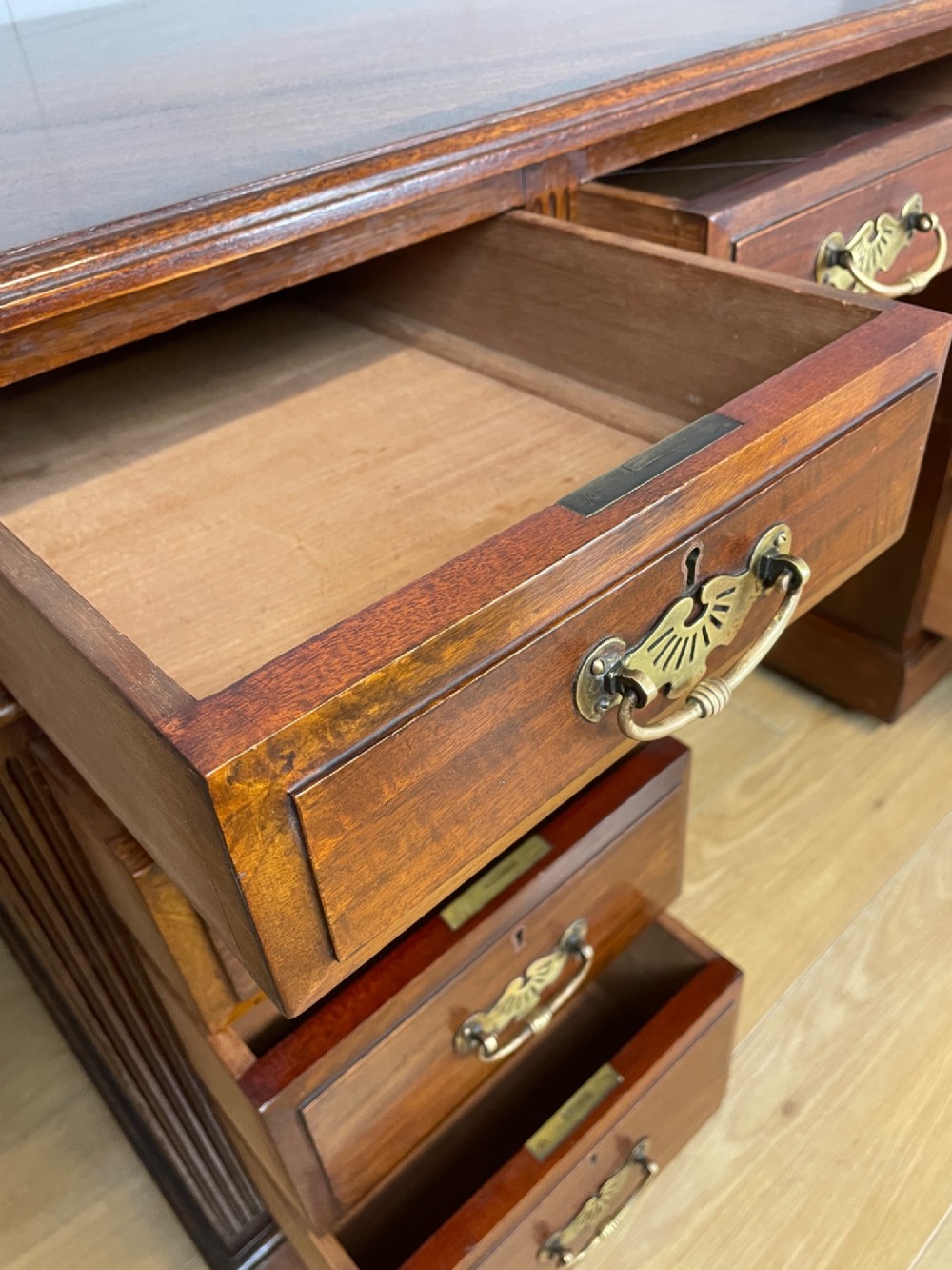 A nineteenth-century mahogany twin pedestal desk featuring nine drawers with brass swan-neck handles and a rectangular veneered top surface. View V