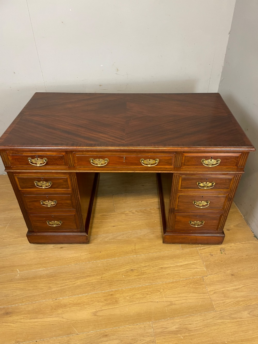 A nineteenth-century mahogany twin pedestal desk featuring nine drawers with brass swan-neck handles and a rectangular veneered top surface. View XI