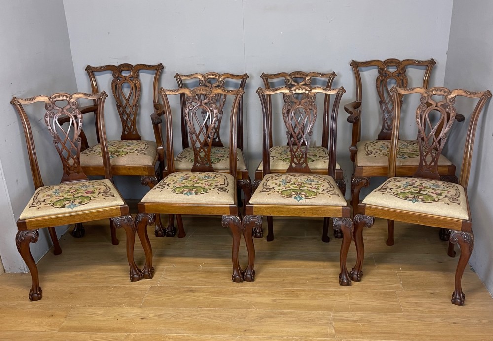 A set of eight dark mahogany Chippendale Revival dining chairs featuring carved pierced back splats, tapestry seat pads, and cabriole legs with ball and claw feet.