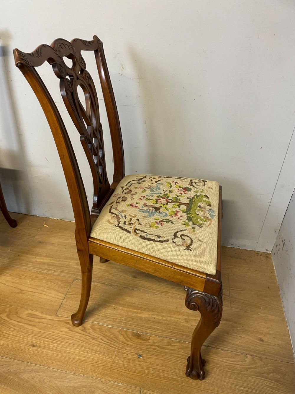 A set of eight dark mahogany Chippendale Revival dining chairs featuring carved pierced back splats, tapestry seat pads, and cabriole legs with ball and claw feet. View X
