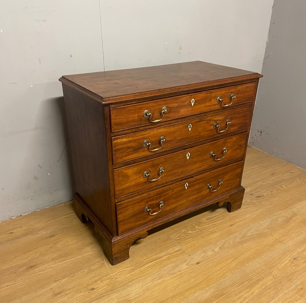 A George III period mahogany chest of drawers featuring four graduated drawers with brass swan-neck handles, diamond keyhole escutcheons, and bracket feet. View II
