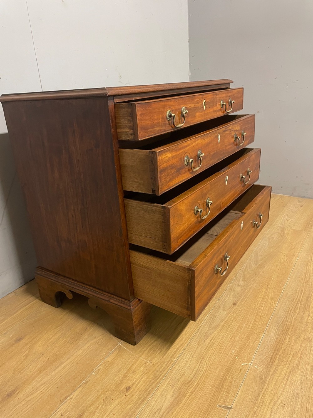 A George III period mahogany chest of drawers featuring four graduated drawers with brass swan-neck handles, diamond keyhole escutcheons, and bracket feet. View V