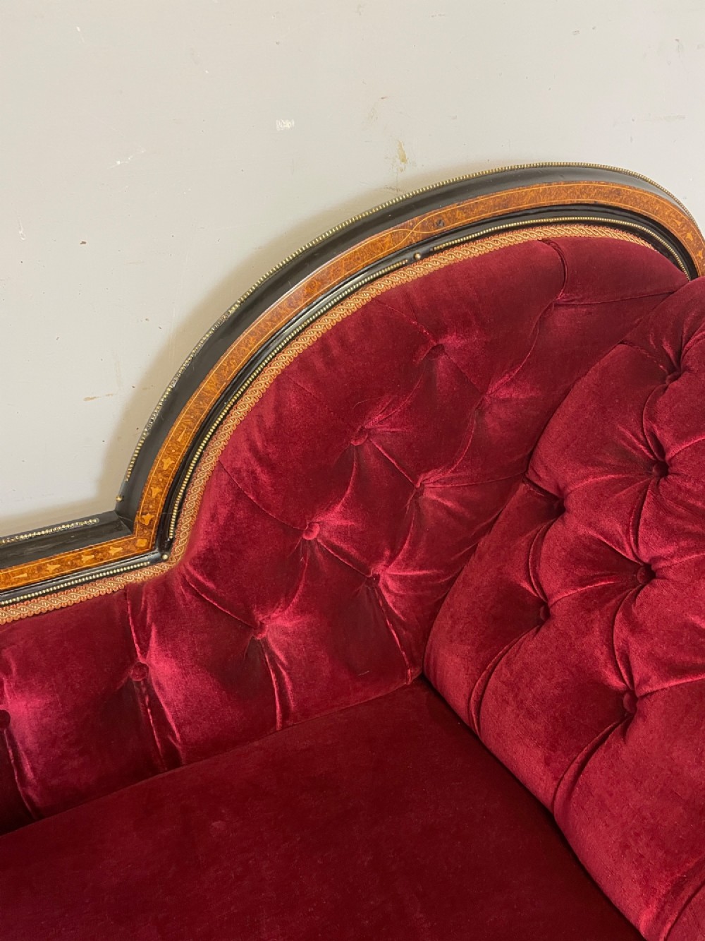 A 19th-century ebonised chaise longue with deep red velvet tufted upholstery, walnut inlaid borders, turned legs on brass castors, and decorative ormolu mounts. View IV