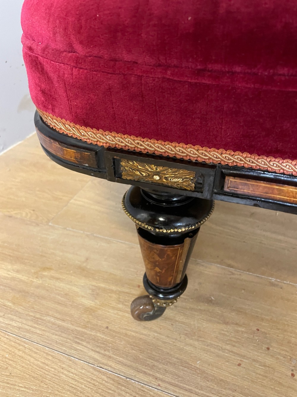 A 19th-century ebonised chaise longue with deep red velvet tufted upholstery, walnut inlaid borders, turned legs on brass castors, and decorative ormolu mounts. View VI