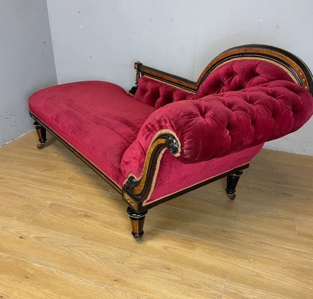 A 19th-century ebonised chaise longue with deep red velvet tufted upholstery, walnut inlaid borders, turned legs on brass castors, and decorative ormolu mounts. View VIII