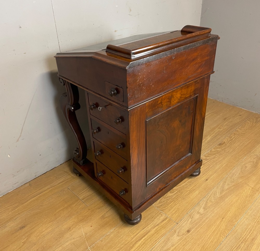 A late 19th-century walnut Davenport desk featuring a sloped leather writing top, carved cabriole front supports, and side drawers. View X