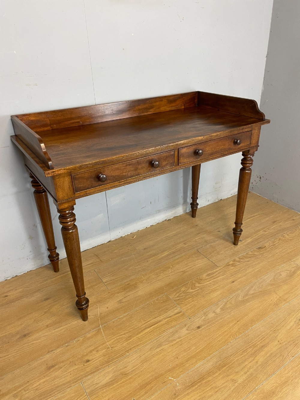 A nineteenth-century flame mahogany side table featuring a three-sided gallery top, two inline drawers with turned knobs, and four turned legs.