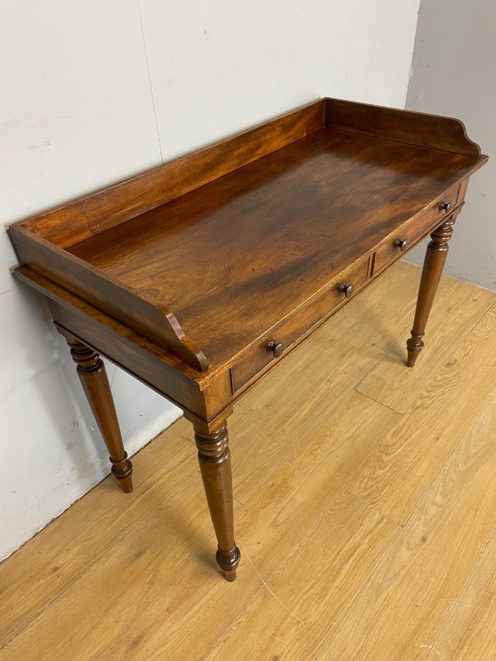 A nineteenth-century flame mahogany side table featuring a three-sided gallery top, two inline drawers with turned knobs, and four turned legs. View II