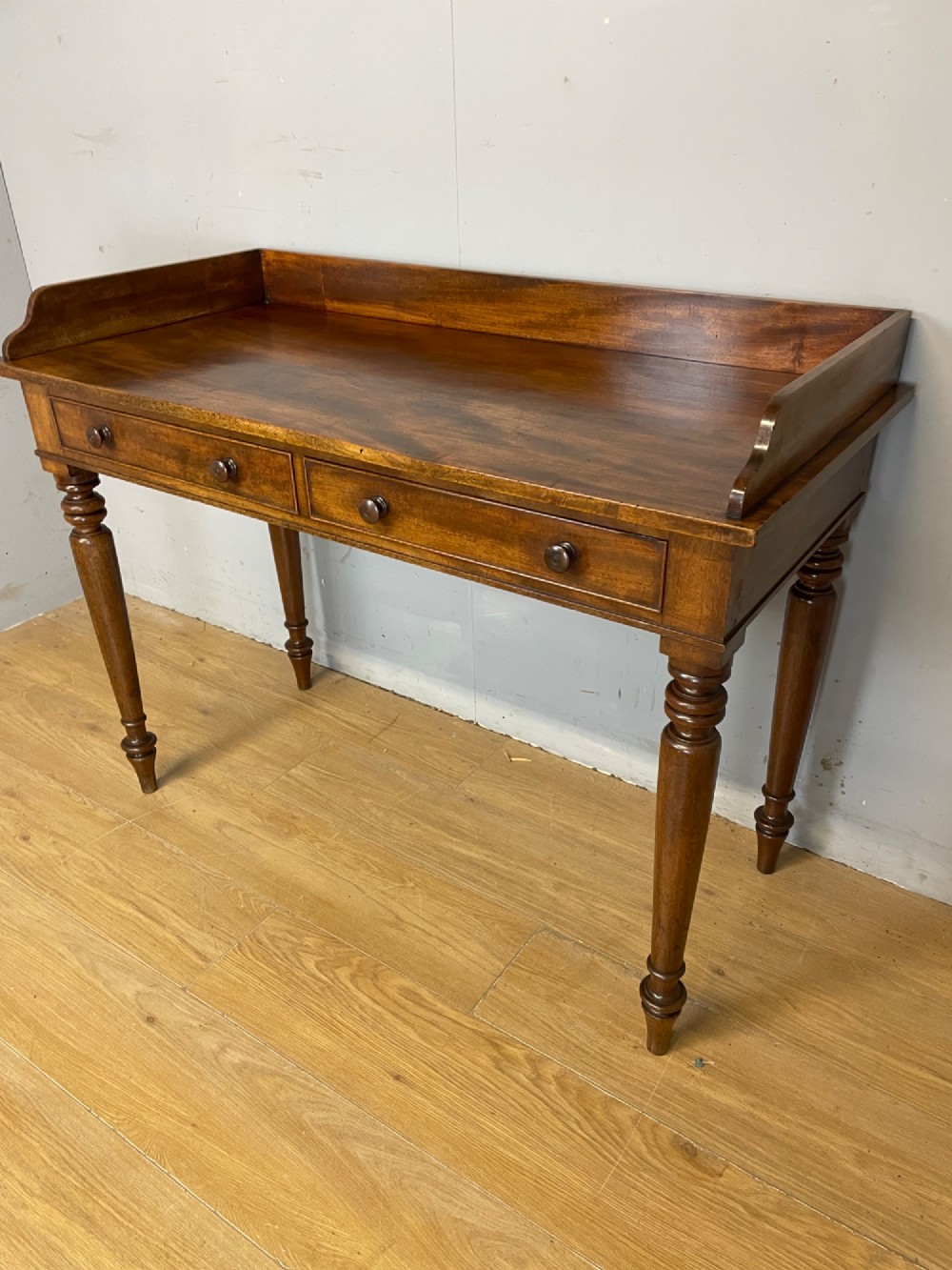A nineteenth-century flame mahogany side table featuring a three-sided gallery top, two inline drawers with turned knobs, and four turned legs. View IV